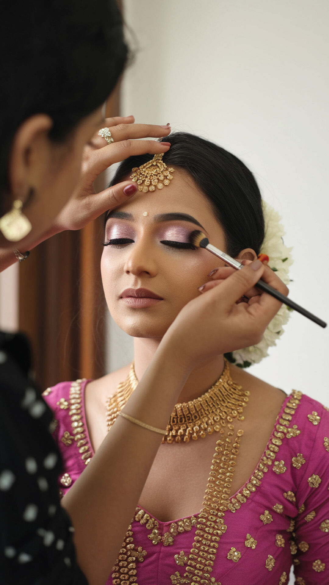 Bride getting makeup done with matching pink bridal wear by professional makeup artist